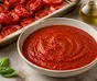 Skål med glatt rød tomatsaus, omgitt av ovnsbakte tomater, hvitløk og basilikum